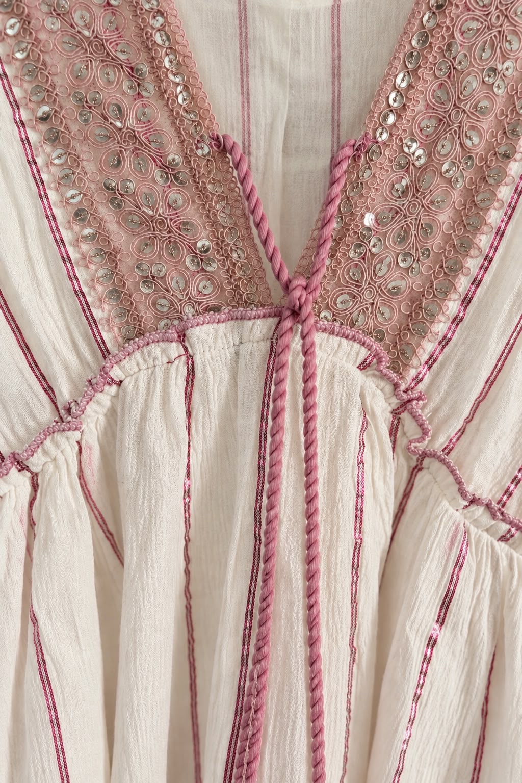 Detalle del escote en V bordado con lentejuelas del vestido rosa y blanco