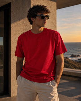 Hombre con remera básica roja, pantalón claro y lentes de sol frente al mar